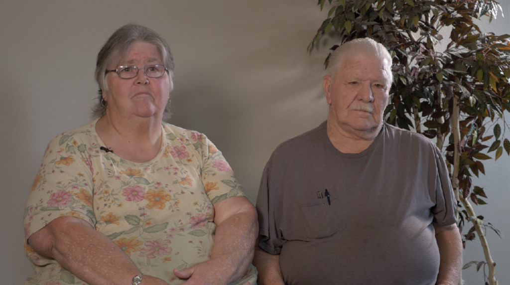 Image of an older man and woman sitting next to a potted plant.