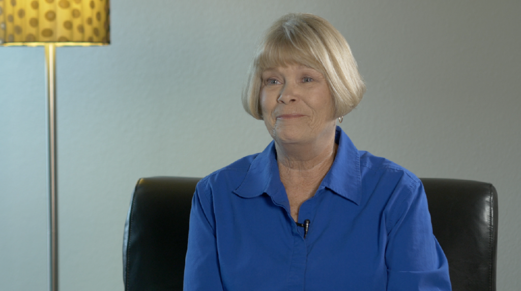 Image of a blonde woman in a blue shirt sitting next to a lamp.