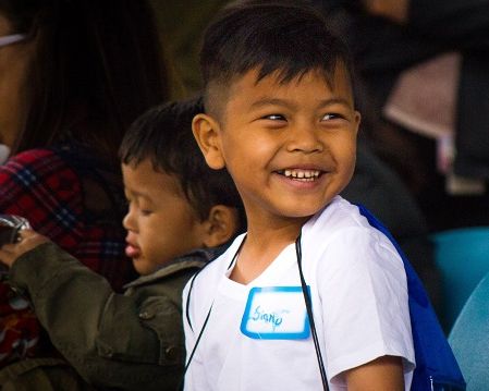 Image of a smiling brown-skinned boy in a white t-shirt.