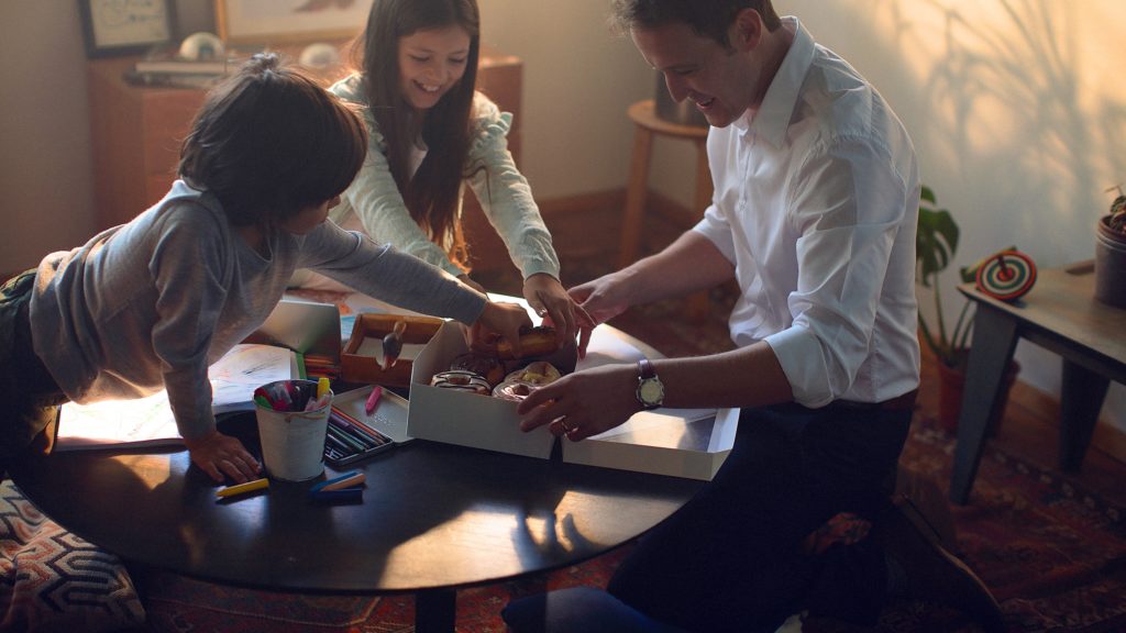 Image of a smiling family reaching into a box of donuts.