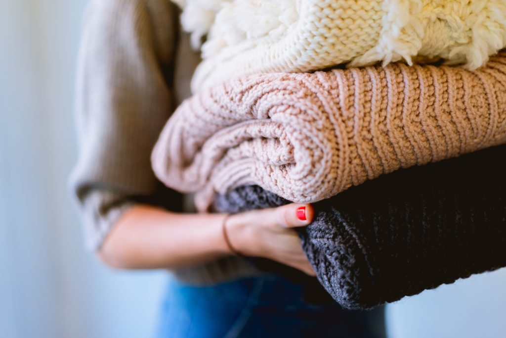 Image of a person holding a stack of folded blankets and sweaters.