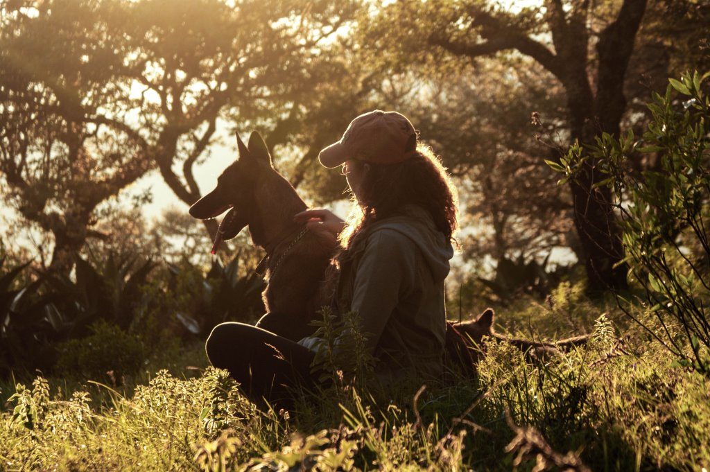 Image of a woman in a baseball cap and her dog sitting in front of trees.