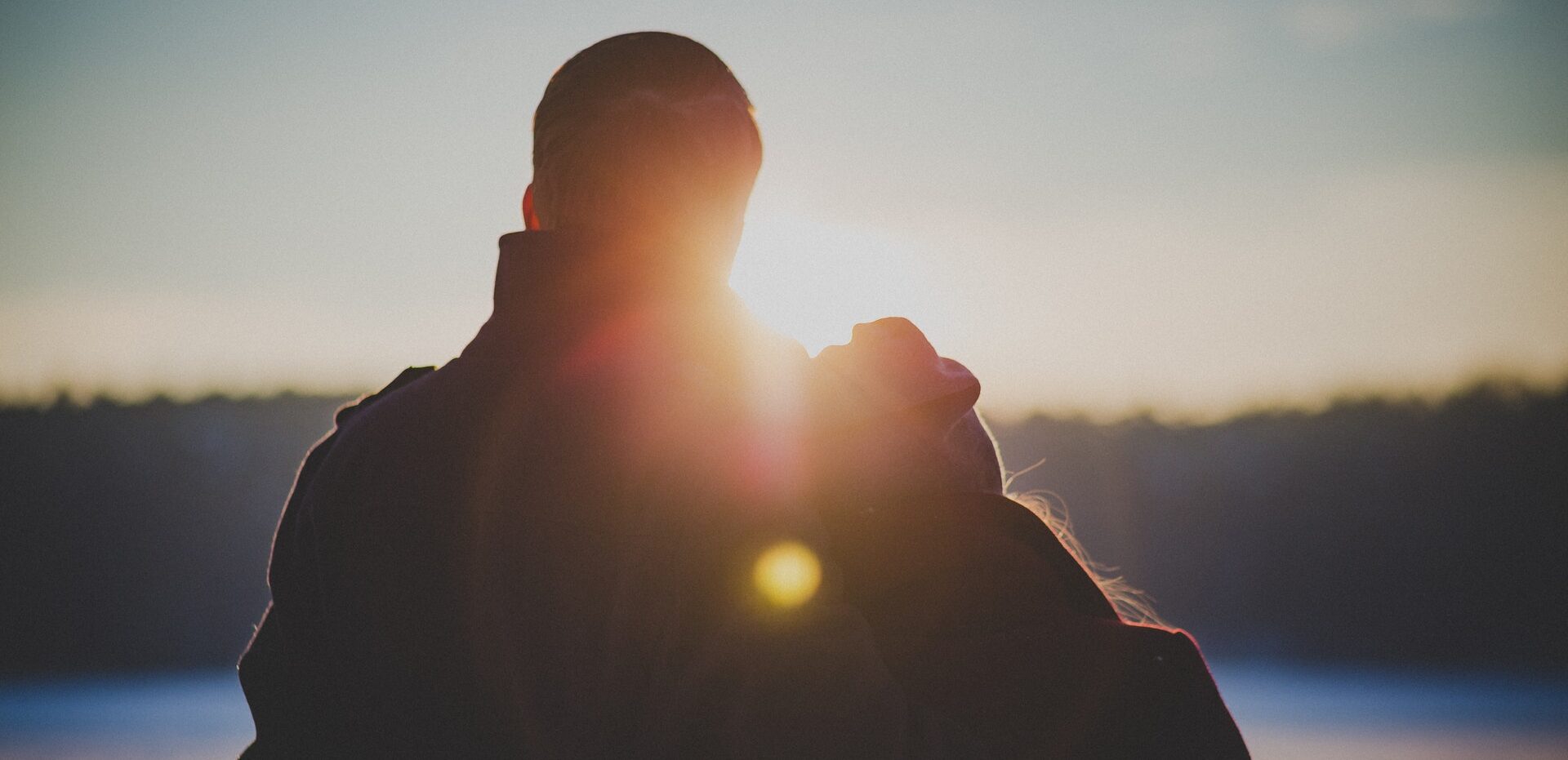 A backlit couple in winter clothes watches the sunset